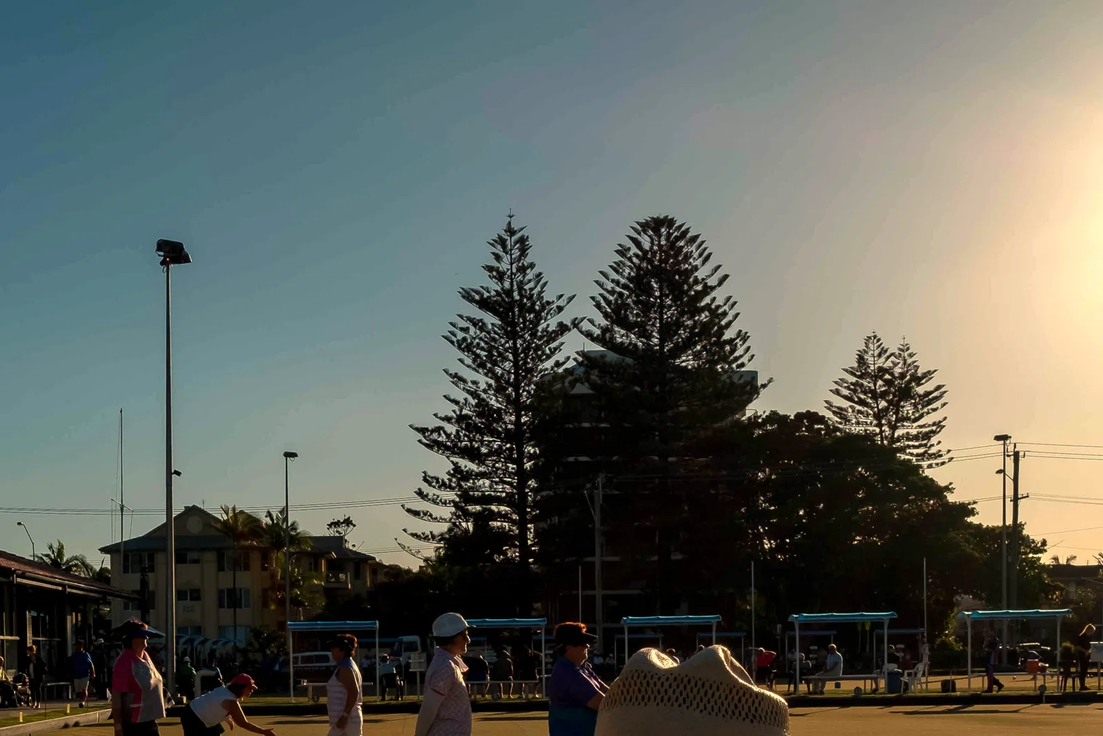 Golden-hour sun over the green with bowlers and spectators